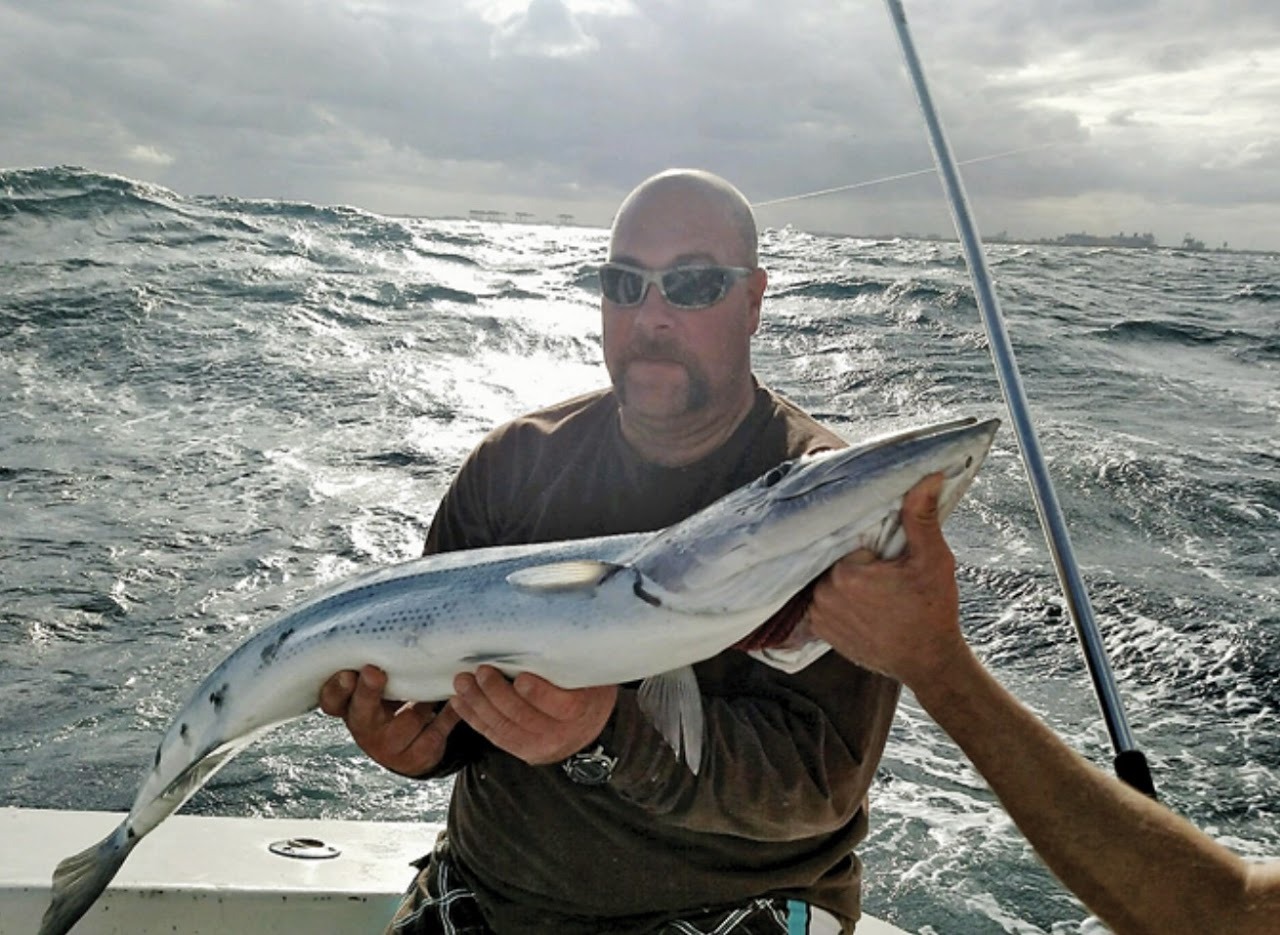 An angler holding a fish above the boat’s wake