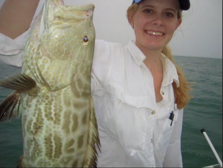 An angler in a white shirt with a spotted fish